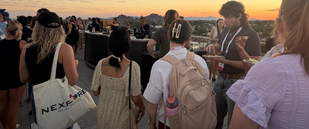 SPARC 2026 attendees mingle on an outdoor terrace at sunset, with a Nexplore tote bag visible in the foreground.